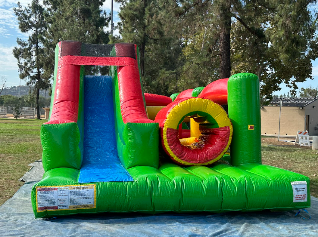 A green and red bouncy house is sitting on top of a tarp in a park.
