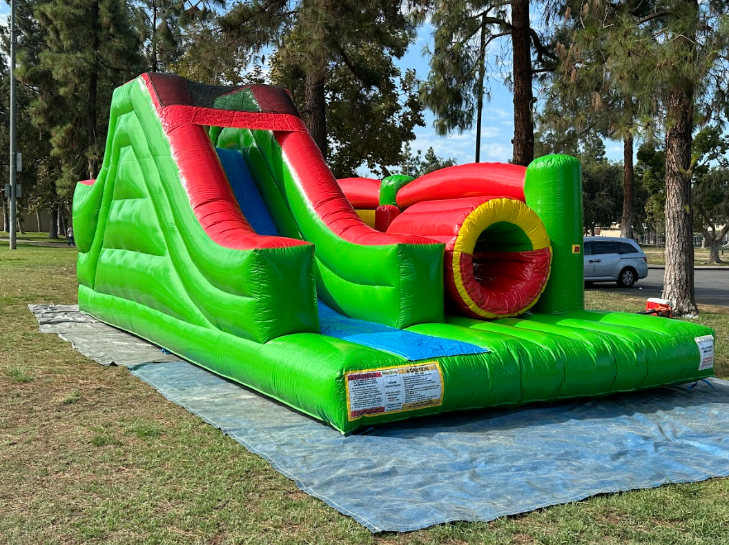 A green and red bouncy house is sitting on top of a tarp in a park.