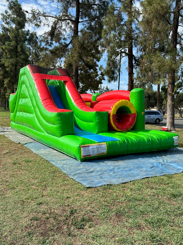 A green and red bouncy house is sitting on top of a tarp in a park.