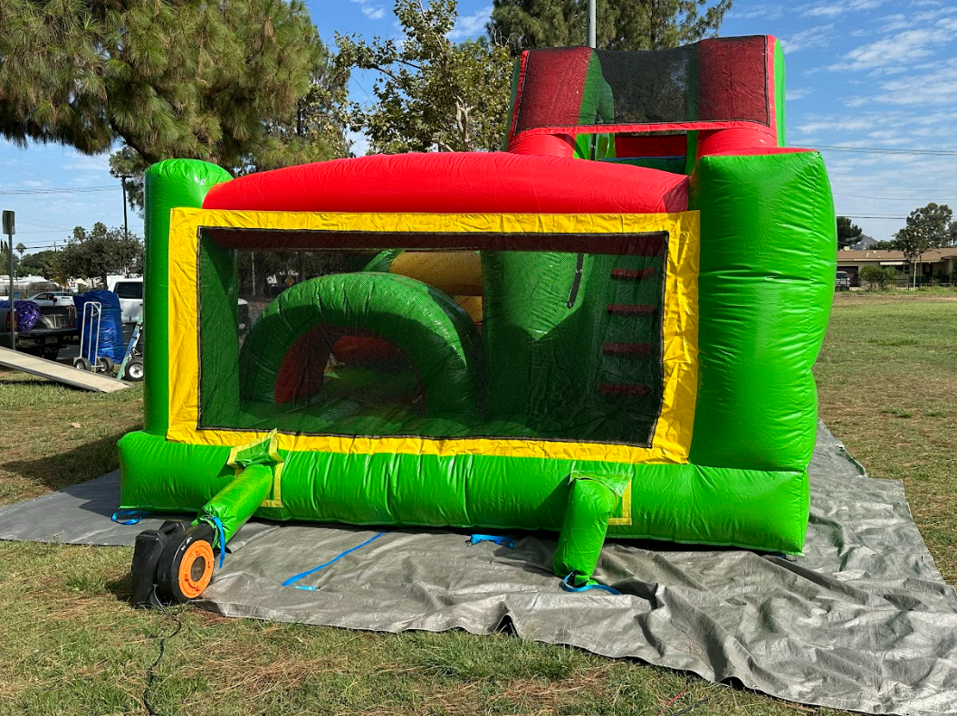 A green and red bouncy house is sitting on top of a blanket in a park.