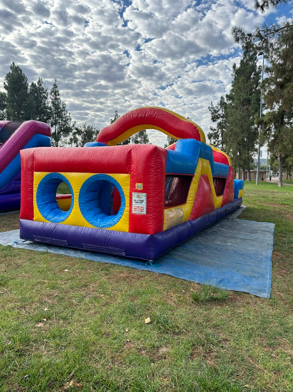 A colorful inflatable obstacle course is sitting on top of a blue tarp in a park.