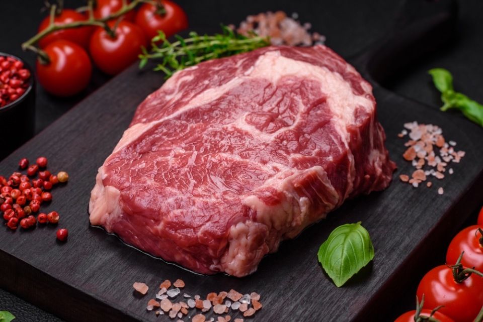 Fresh, raw beef steak with salt, spices and herbs on a dark textured background