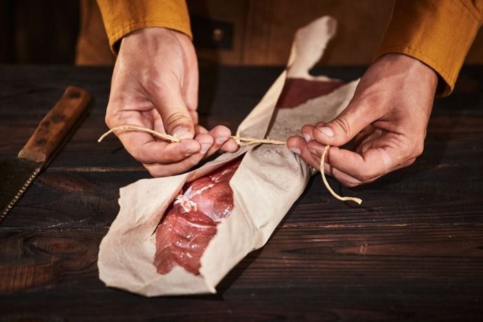The butcher wraps a piece of meat in paper.
