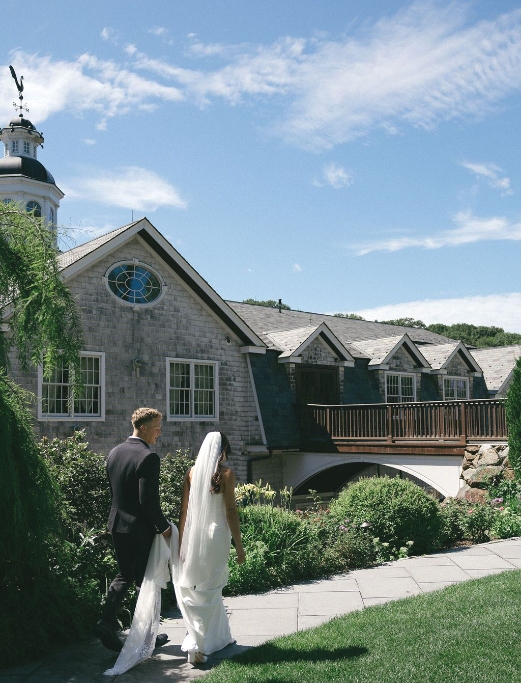 Bride and groom on a wooden deck at The Whittemore, looking at each other. Sunset colors in the sky and a building with gray shingles behind them.