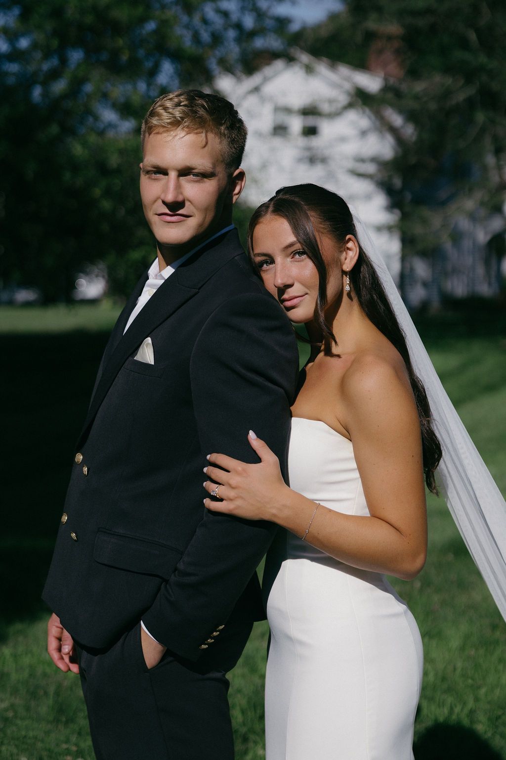 Two women in wedding dresses are hugging each other in front of a bush.