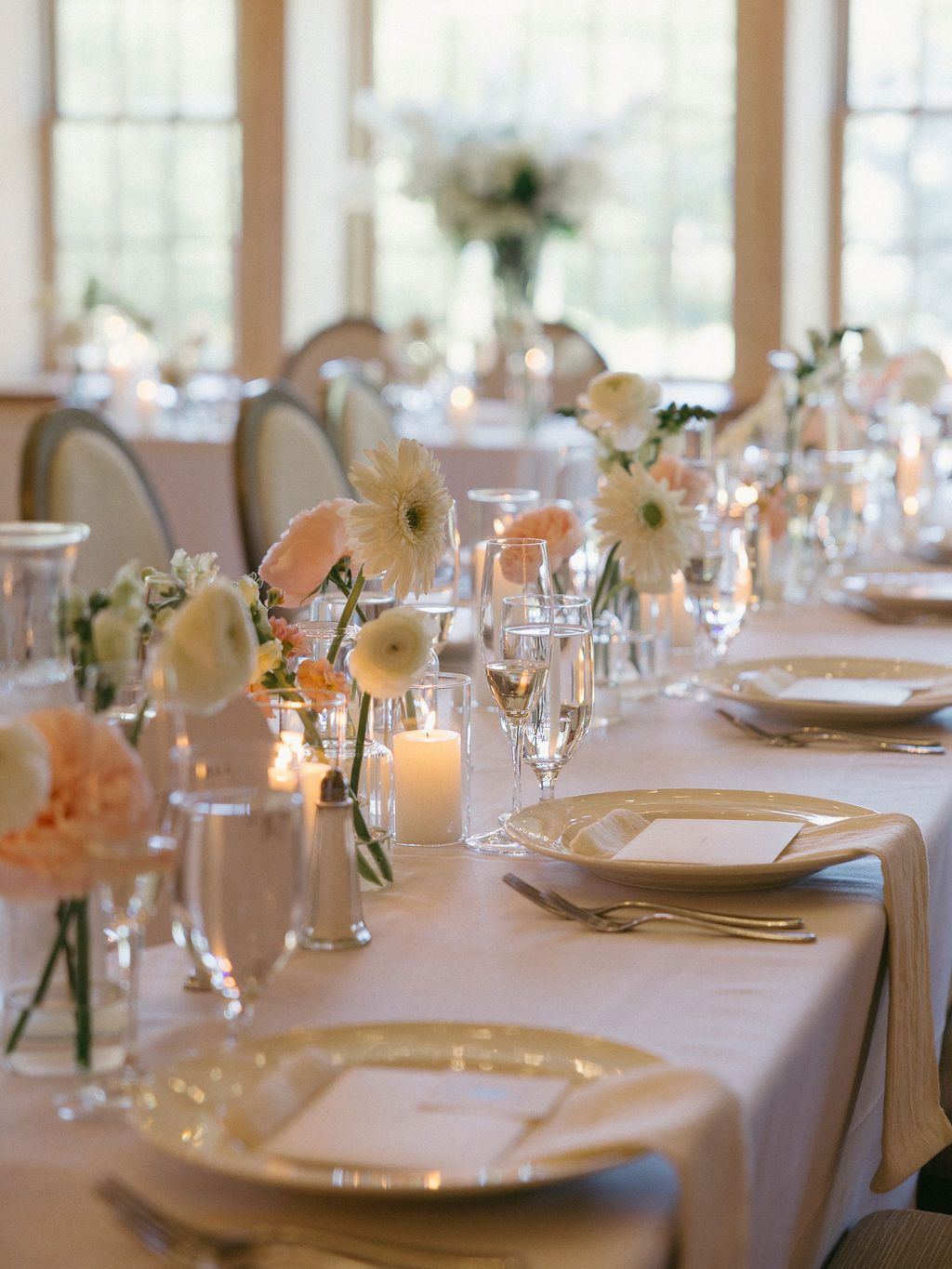 Wedding reception venue with round tables, wooden floors, and a floral archway. The room has light wood beams and a chandelier.