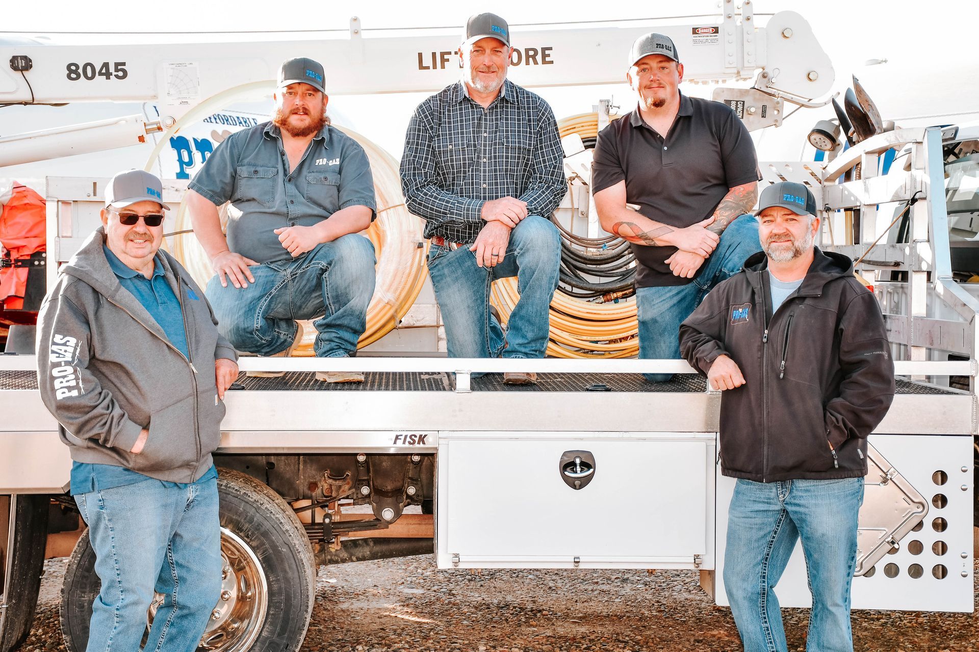 Five men wearing caps and casual attire pose on a truck, likely utility workers.