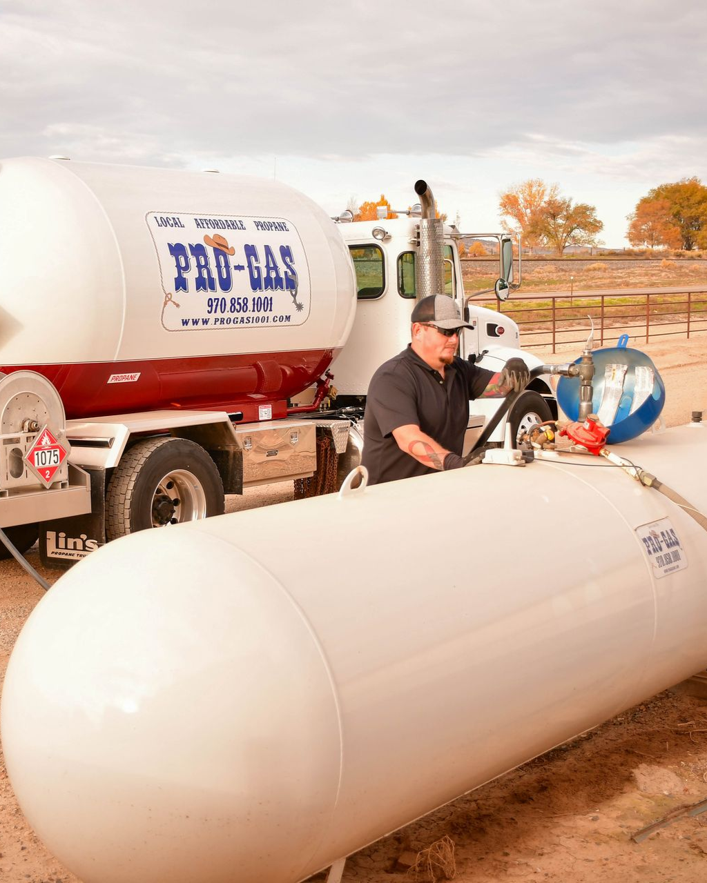 White propane tank next to a service truck, with a colorful desert mountain backdrop.