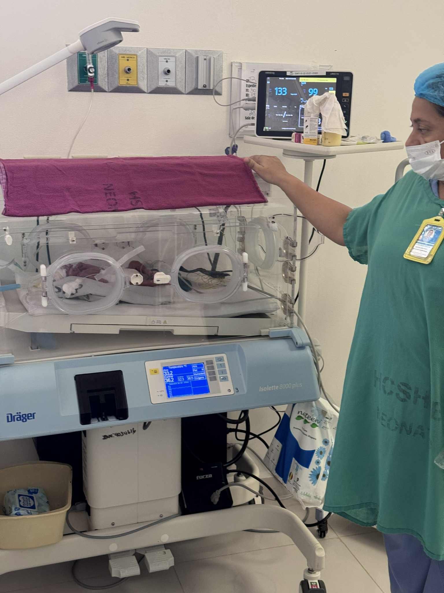 Nurse adjusts the cover of an incubator, a medical device with an infant inside. Hospital setting.
