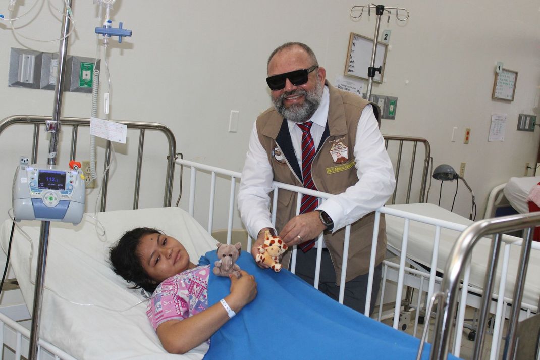 A man is standing next to a little girl in a hospital bed