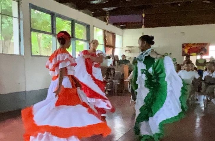 Dancers in colorful ruffled dresses perform in a room with an audience.