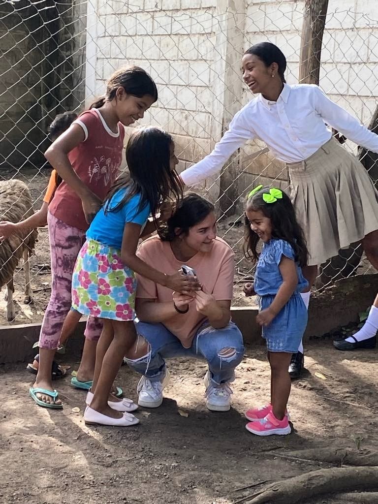 Children and adults interact outdoors by a fence. Smiling and laughing.
