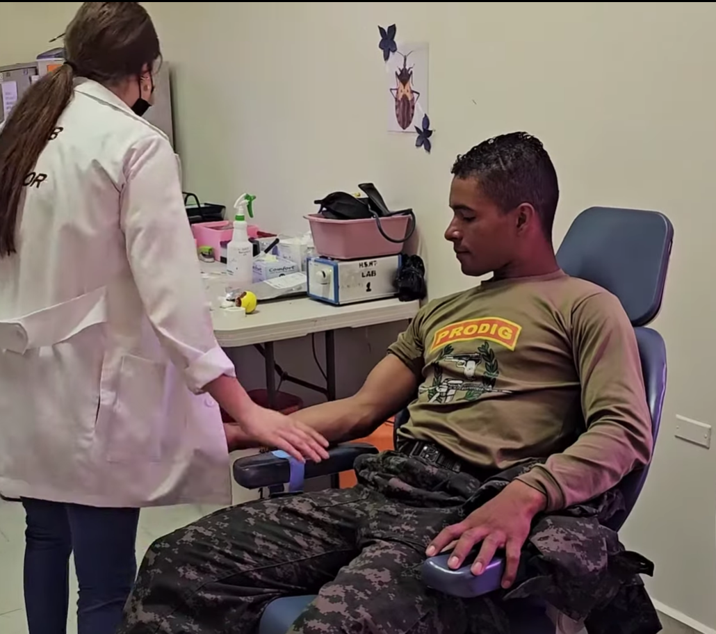 A person sits in a chair as a medical professional prepares to draw blood in a medical setting.