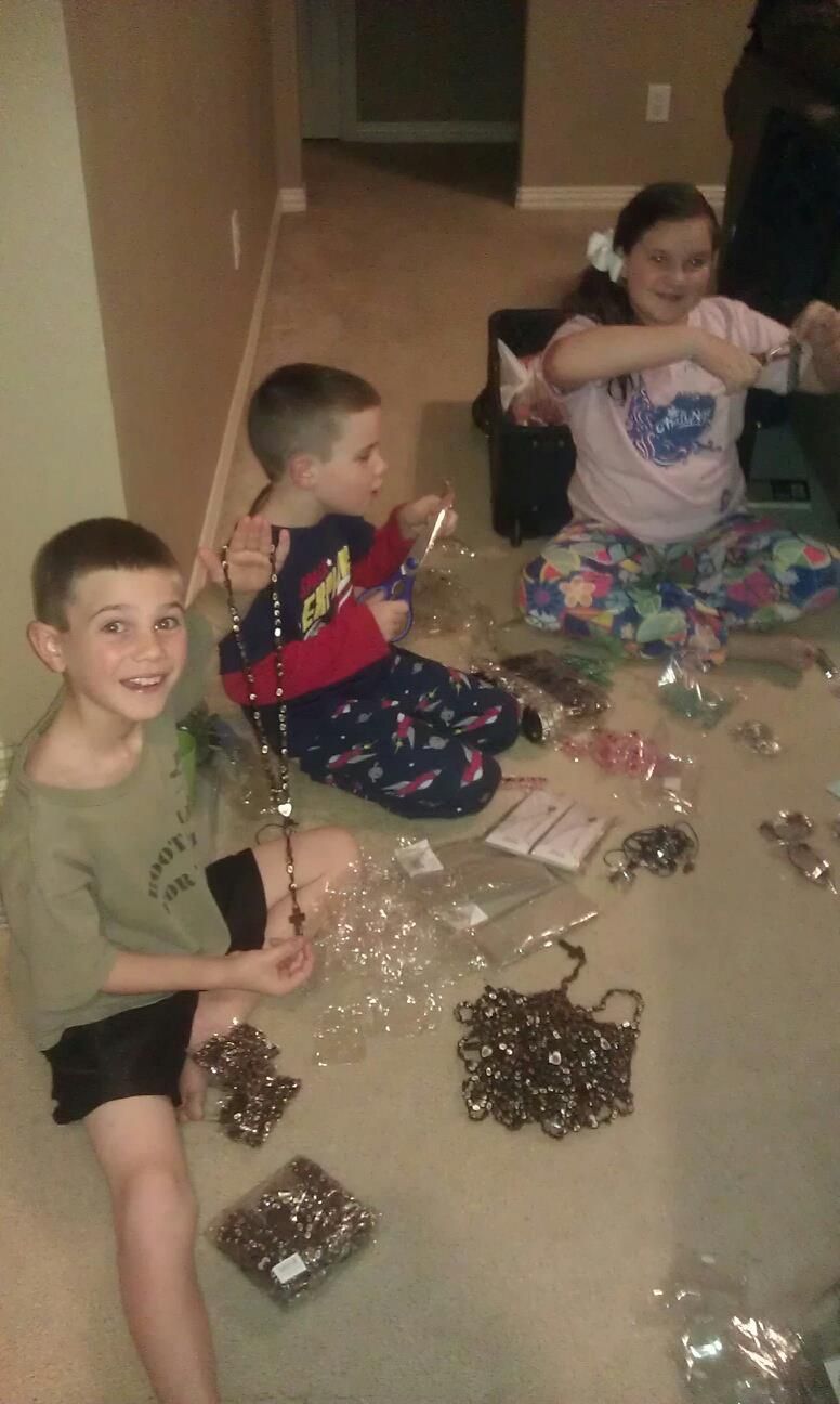 Three children in pajamas sit on a floor surrounded by craft supplies, smiling.