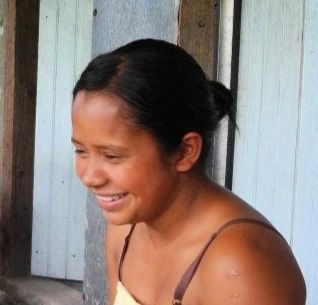 Woman smiling, wearing a tank top, outdoors in front of a wooden wall.
