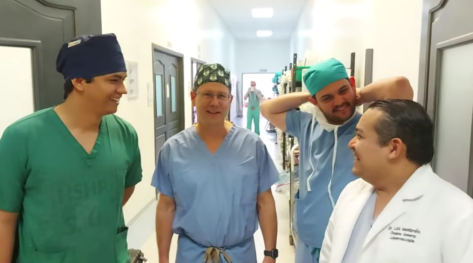 Four medical professionals in scrubs in a hospital hallway, smiling and chatting.