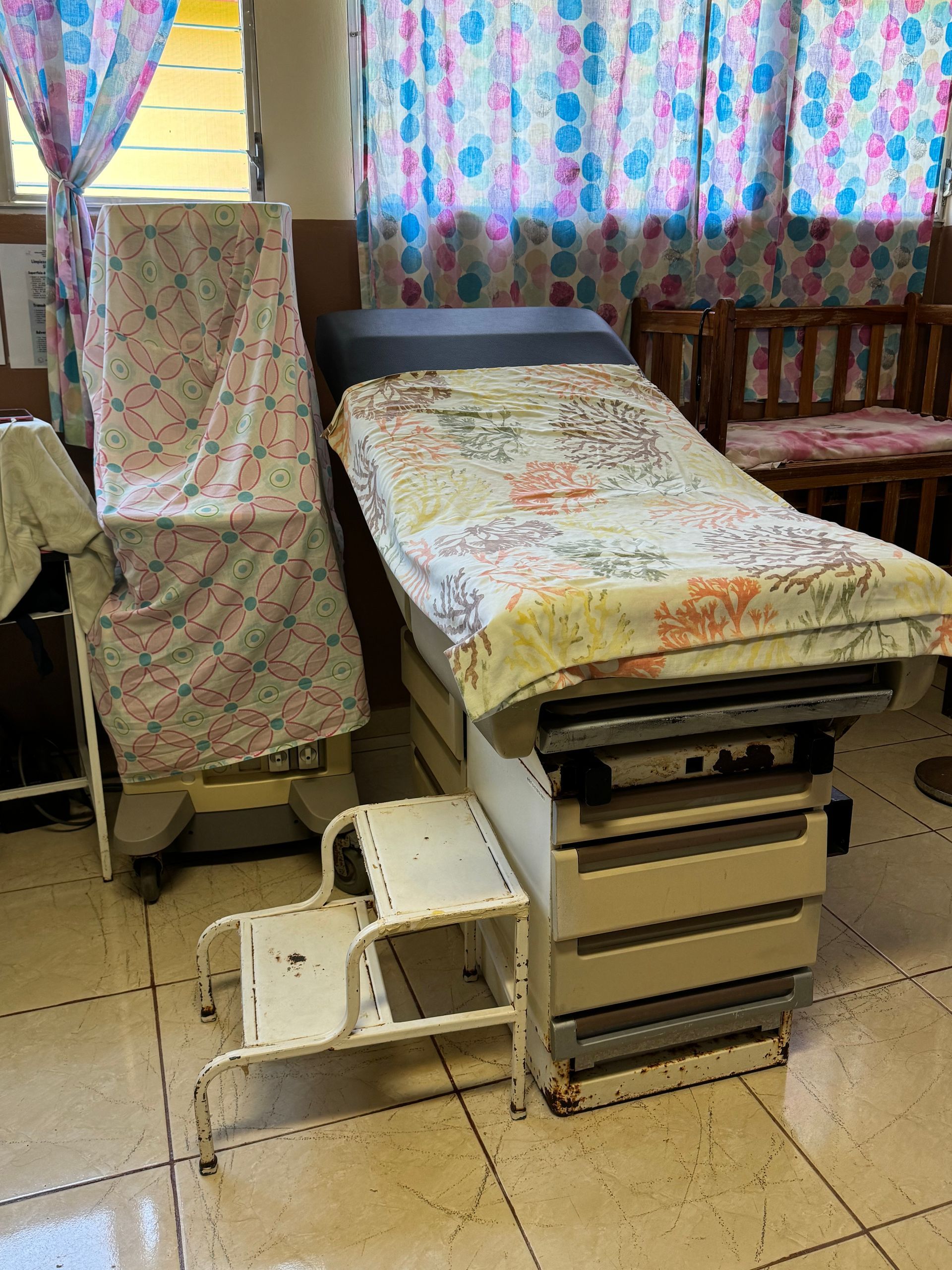 A hospital room with a bed and chairs and a window.