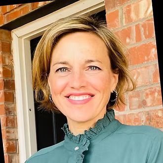 A woman in a green shirt is smiling in front of a brick building.