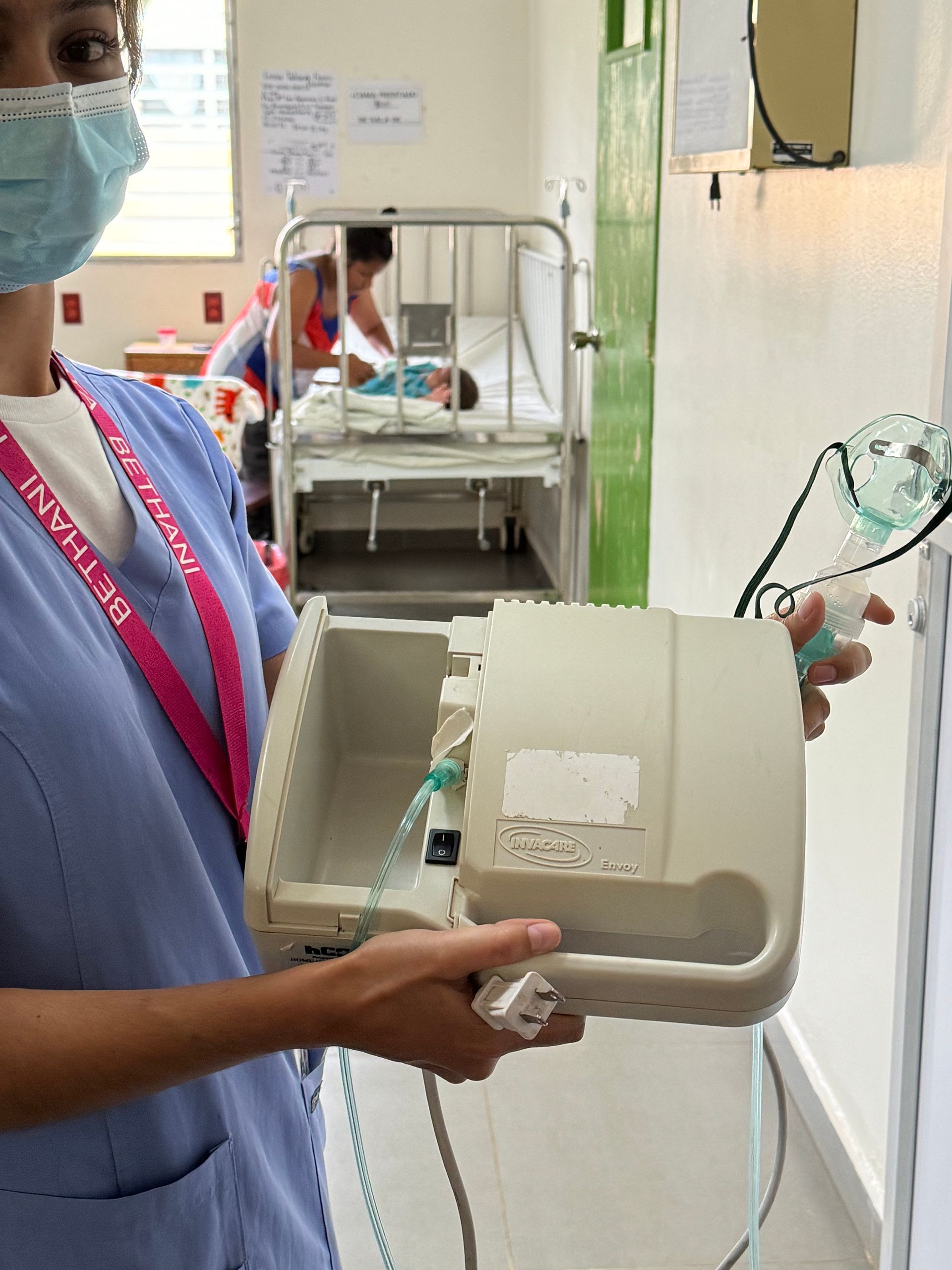 A nurse wearing a mask is holding a device in a hospital room