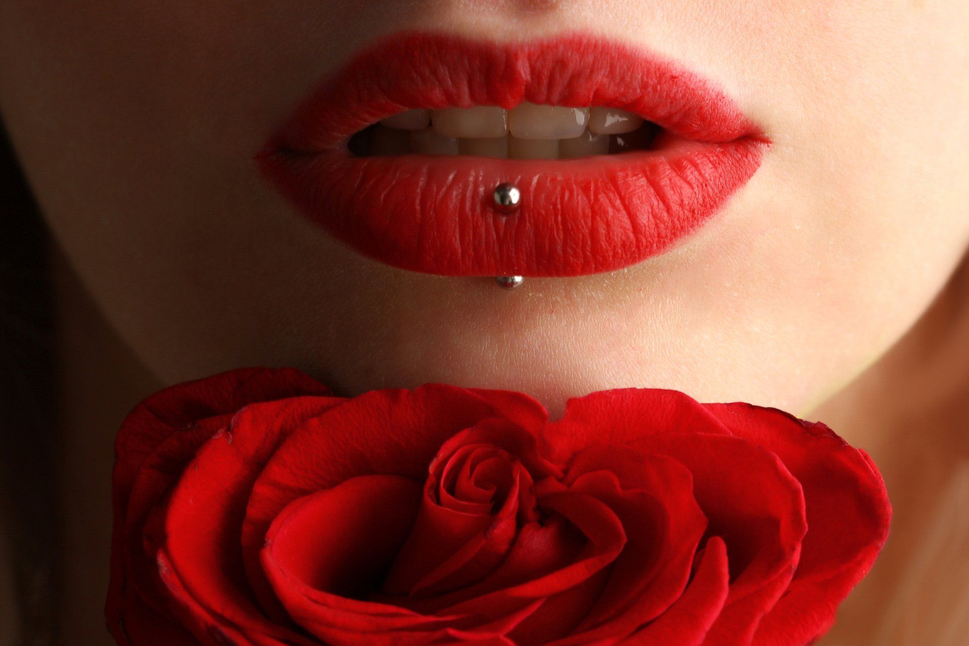 A woman with red lips and a red rose in her mouth