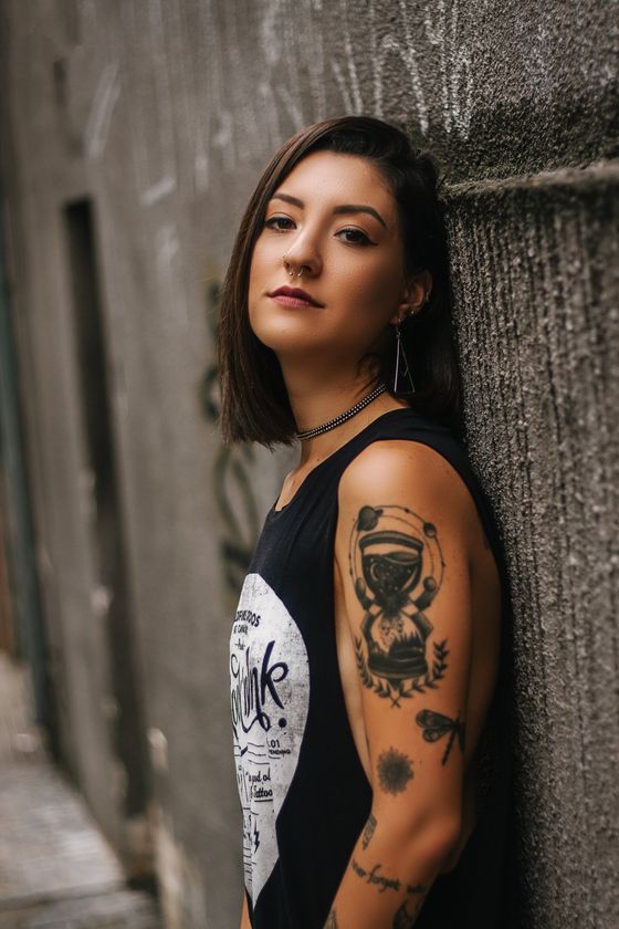 A woman with a lot of tattoos on her arm is leaning against a wall.