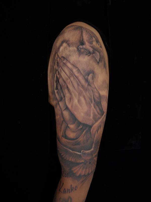 A man has a praying hands tattoo on his arm.
