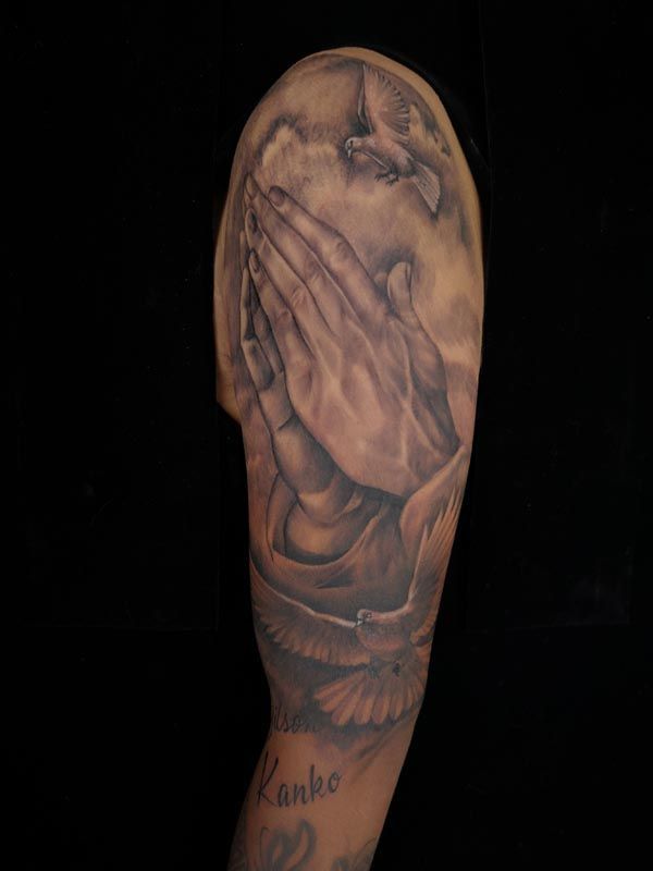 A man has a praying hands tattoo on his arm.