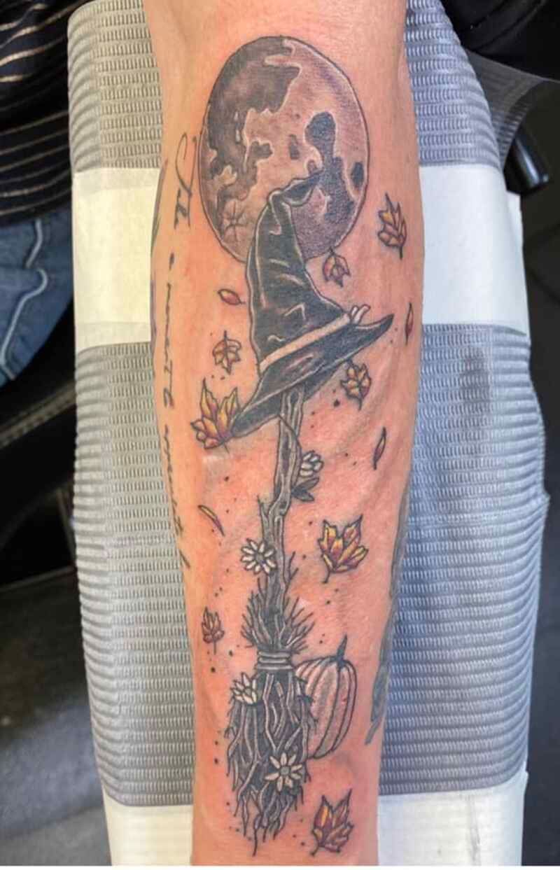 A tattoo of a witch holding a broom with a full moon in the background