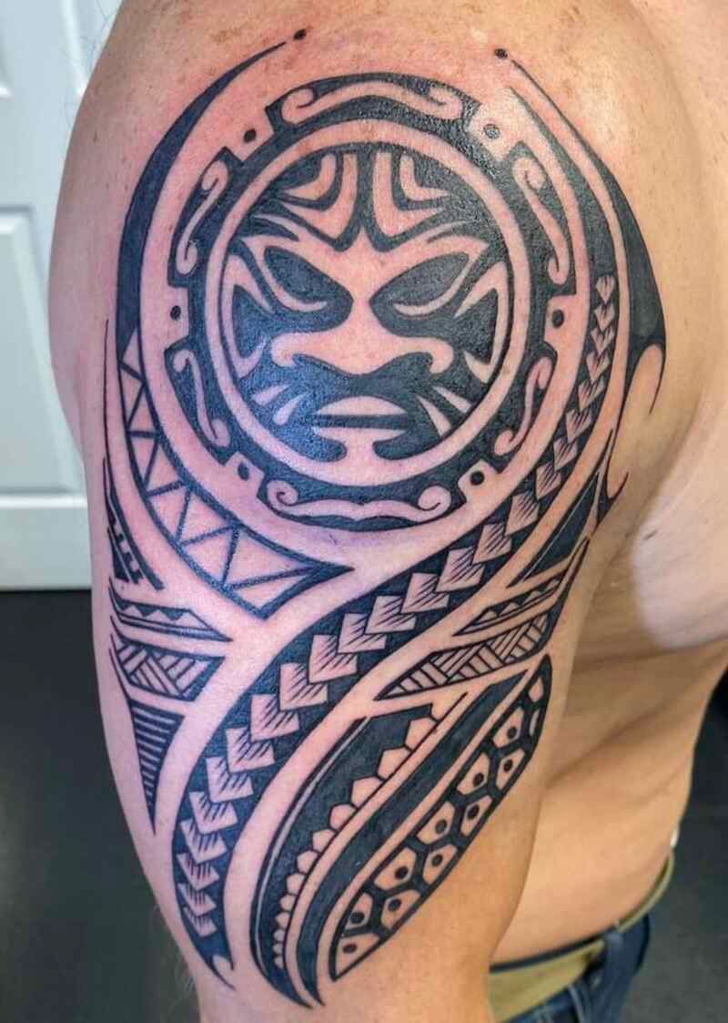 A man has a tribal tattoo on his arm and shoulder