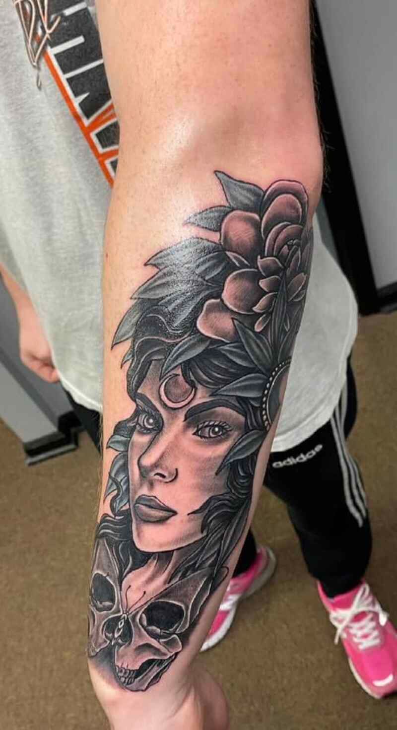 A person has a tattoo of a woman 's face and a skull on their forearm.