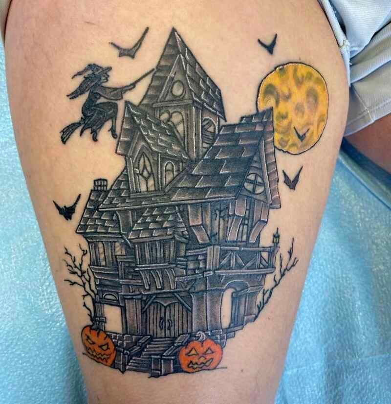 A tattoo of a witch flying over a haunted house with pumpkins and bats.