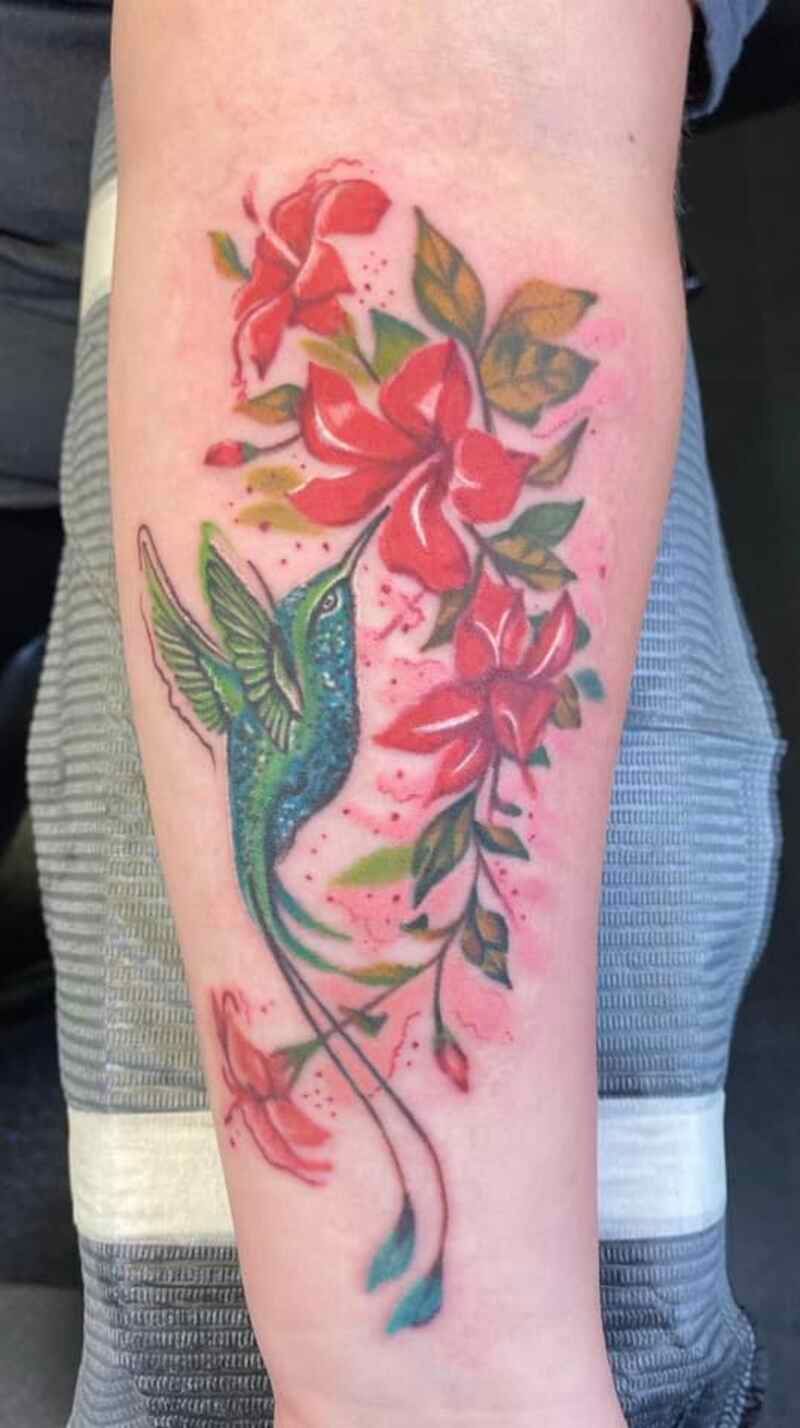 A person has a tattoo of a hummingbird and flowers on their forearm.