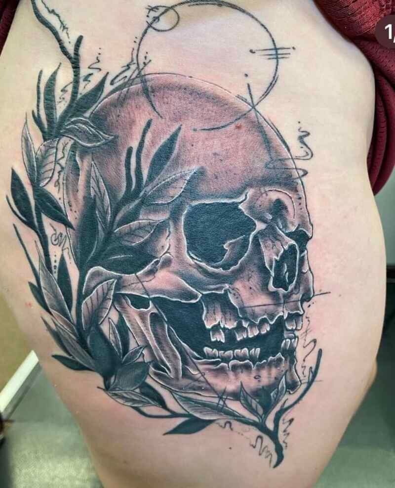 A woman has a tattoo of a skull with leaves around it