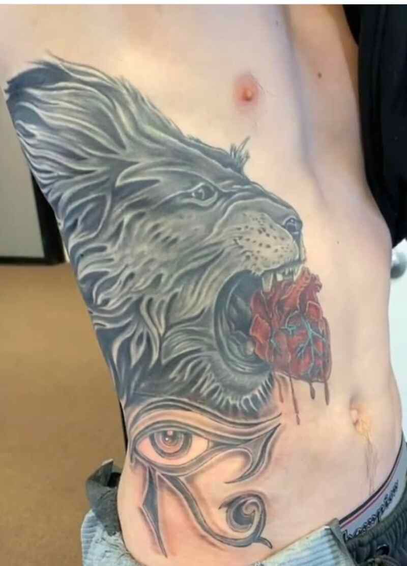 A man has a tattoo of a lion eating a heart on his side.