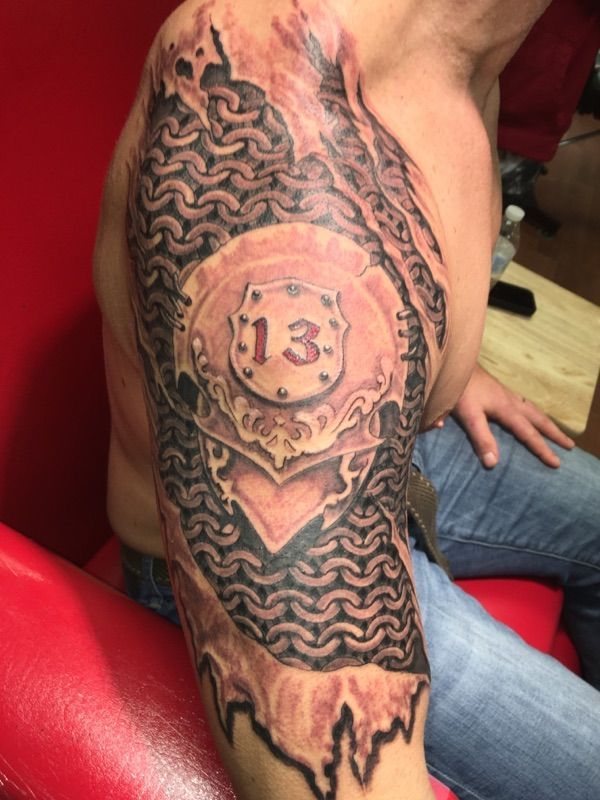 A man has a tattoo of a shield with the number 13 on it.