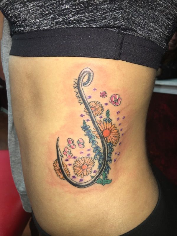 A woman has a tattoo of a fishing hook with flowers around it