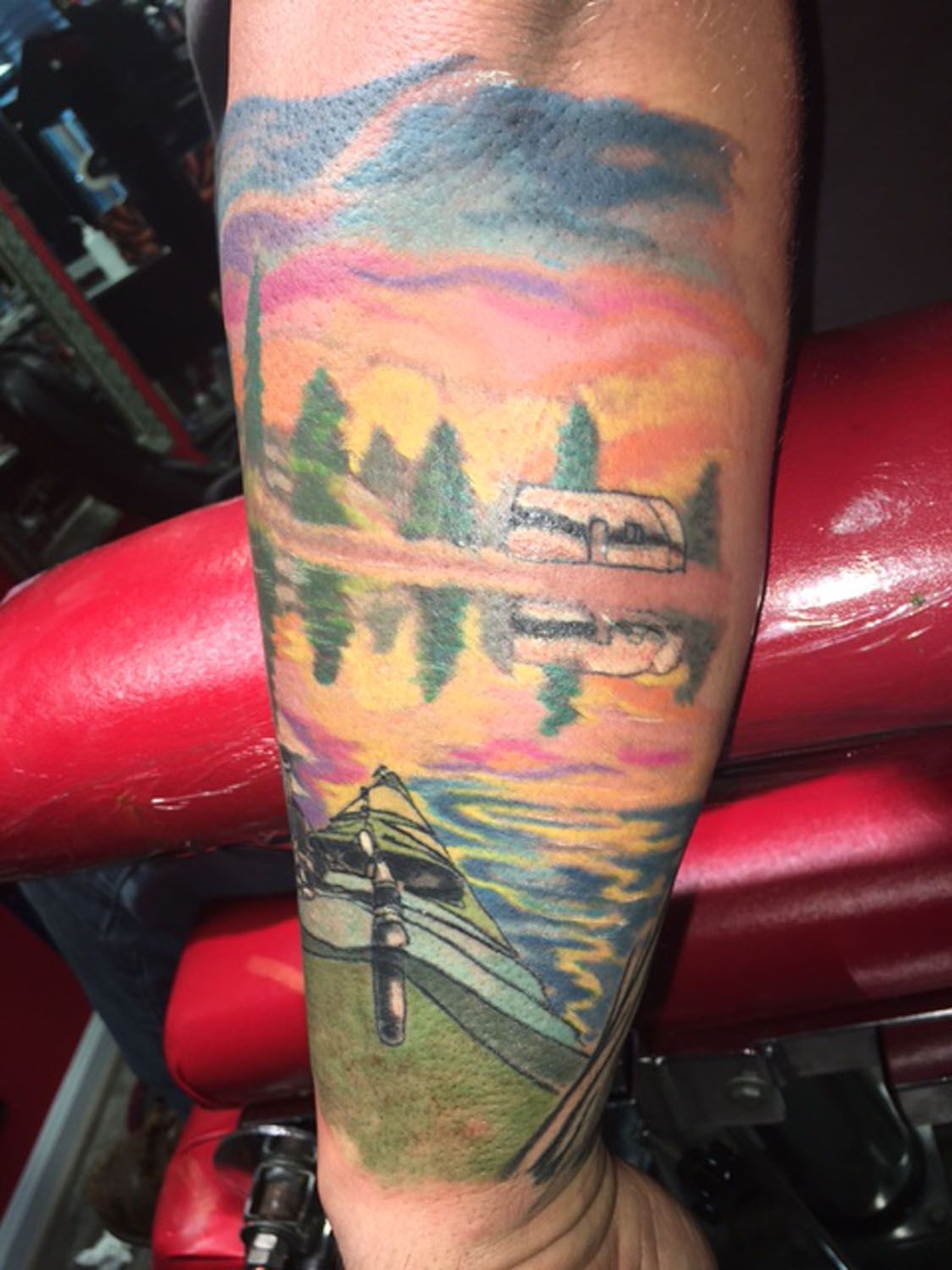A person has a tattoo of a sunset over a lake on their forearm.