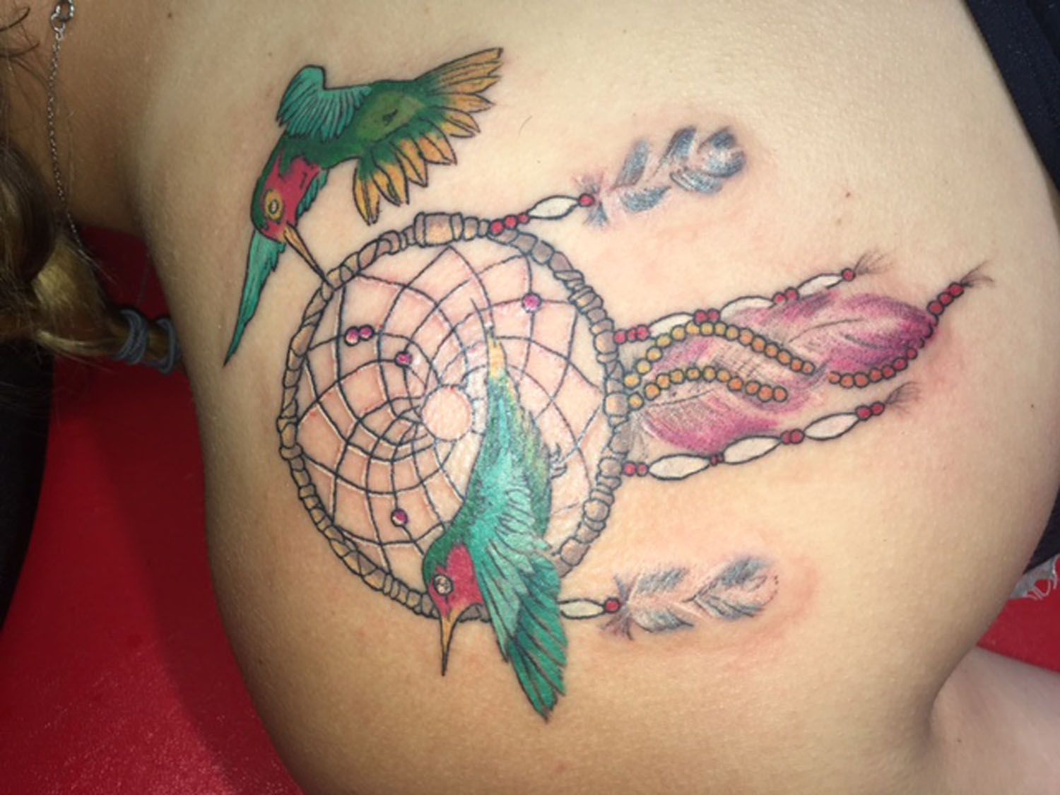 A woman has a tattoo of a hummingbird and a dream catcher on her back