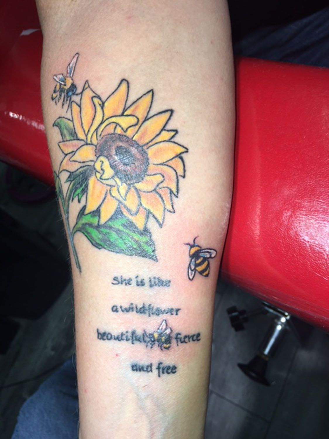 A woman has a tattoo of a sunflower and bees on her forearm