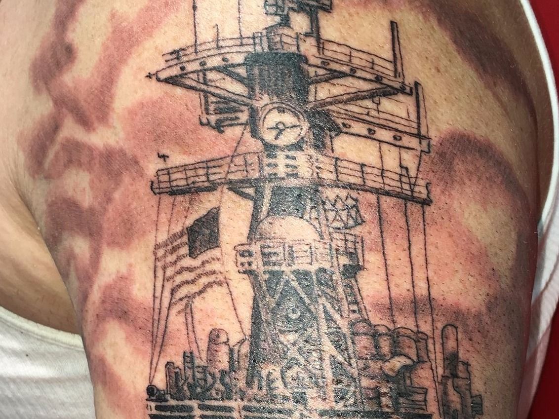 A man has a tattoo of a military ship on his arm.