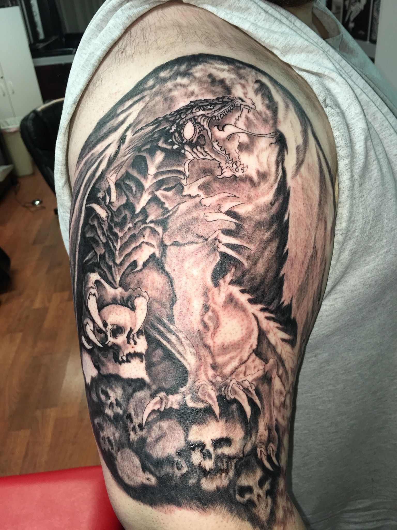 A man has a tattoo of a dragon and skulls on his arm.