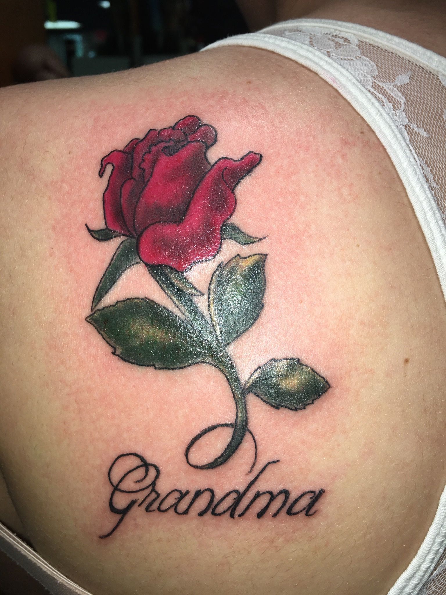 A woman has a tattoo of a red rose and the name grandma on her back.