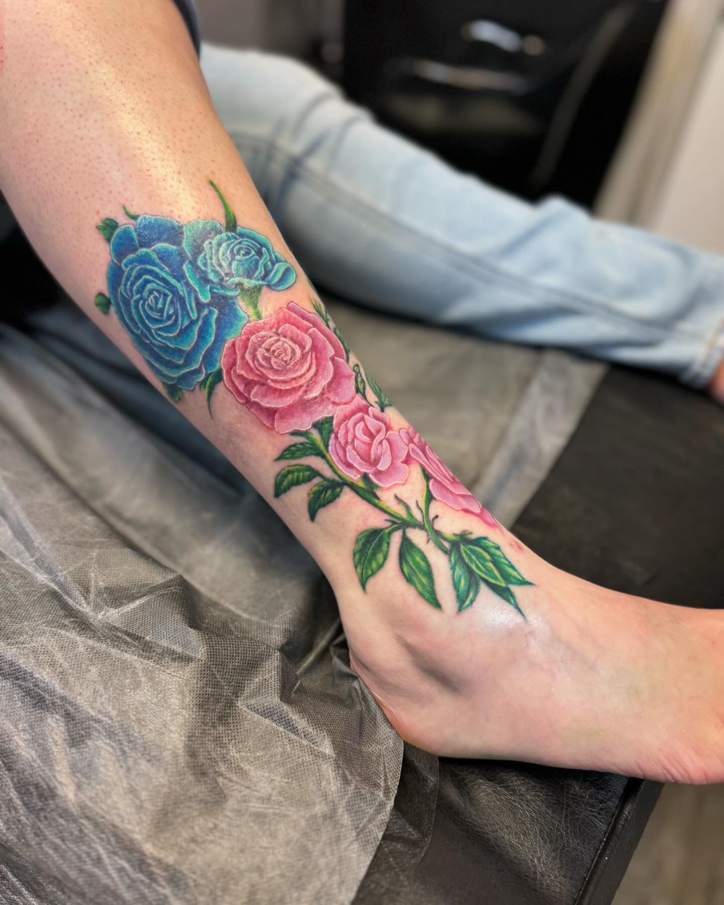 A woman has a tattoo of pink and blue roses on her leg.