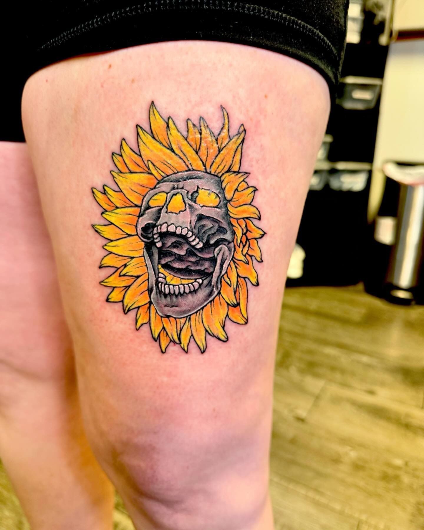 A woman has a tattoo of a skull in a sunflower on her leg.