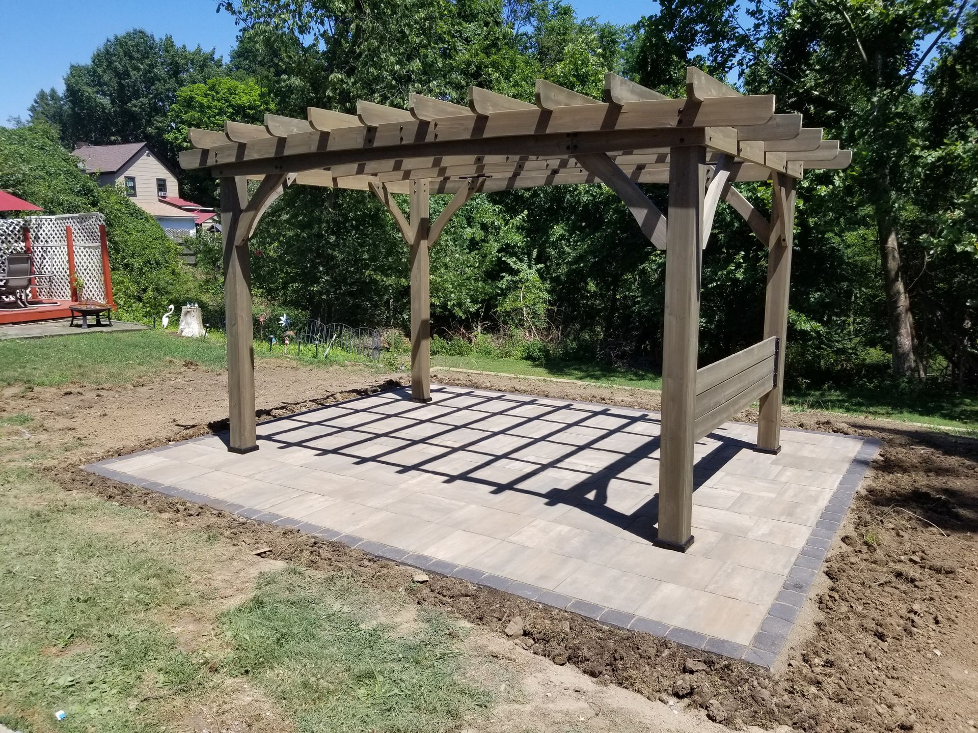 Wooden pergola under construction on a concrete patio in a wooded yard.