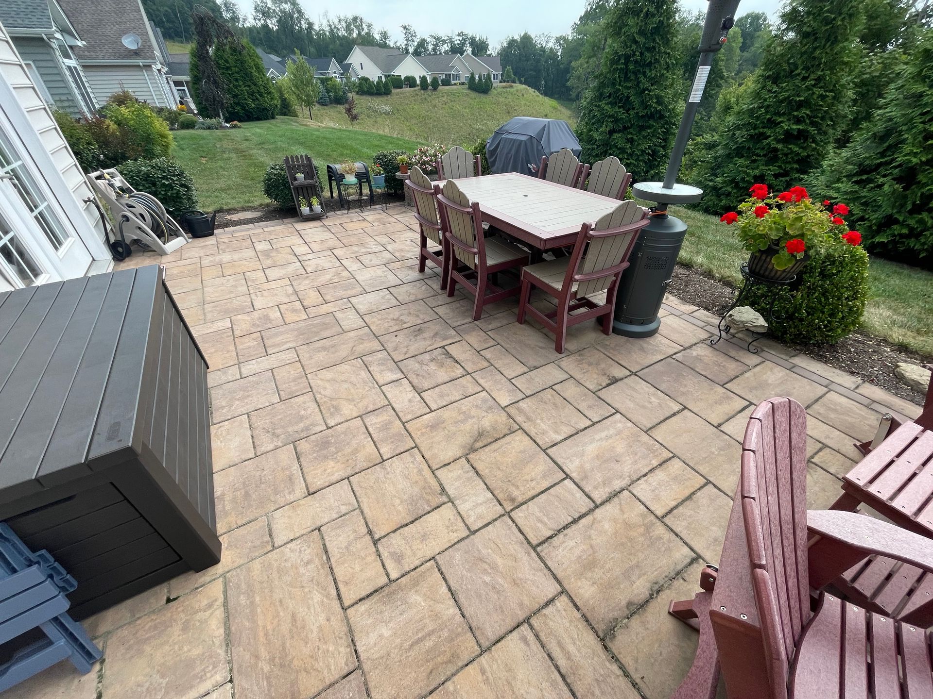 Back patio with tan pavers, table and chairs, planter, storage box, and garden view