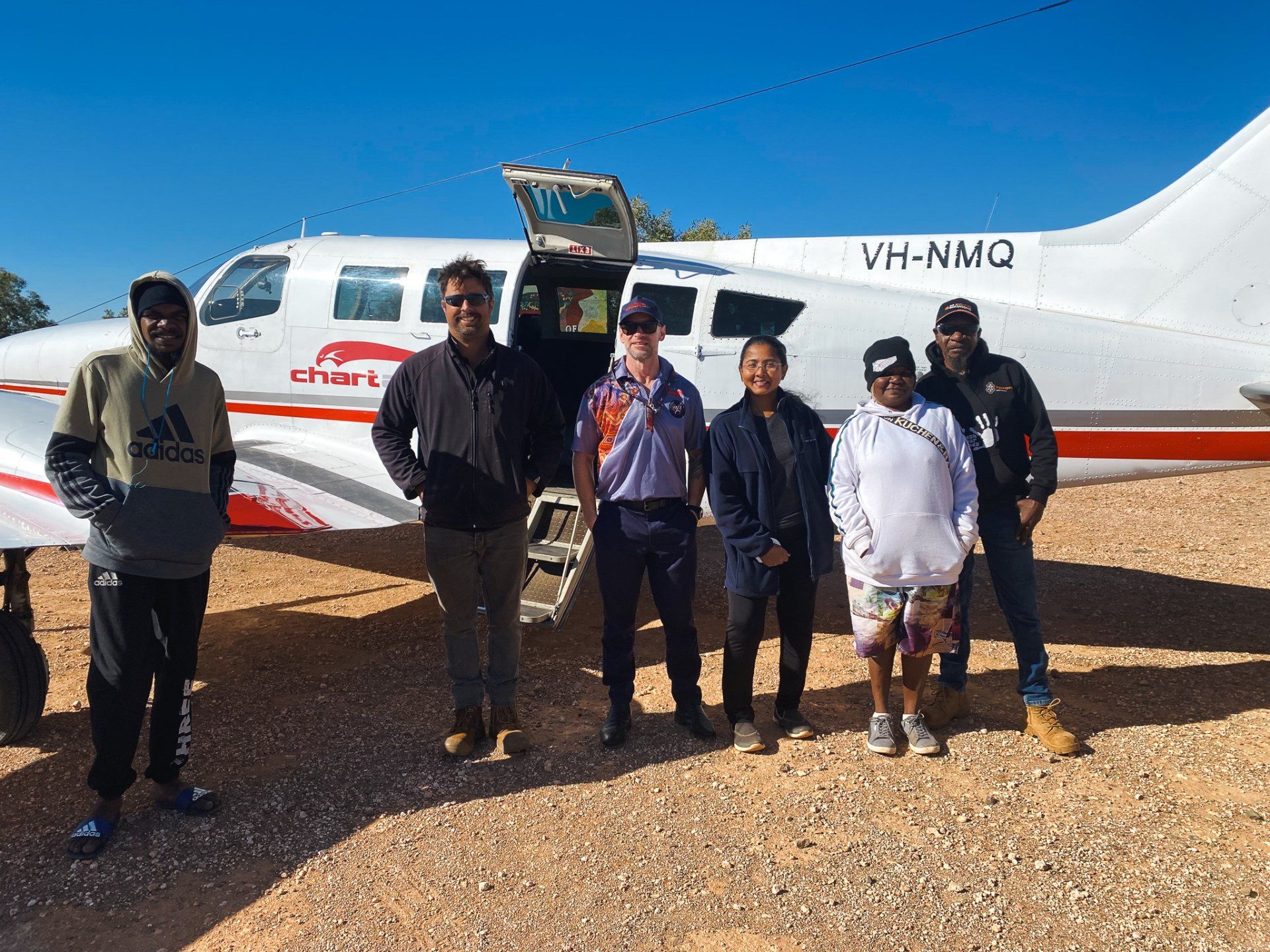 a group of people standing in front of an airplane in remote area