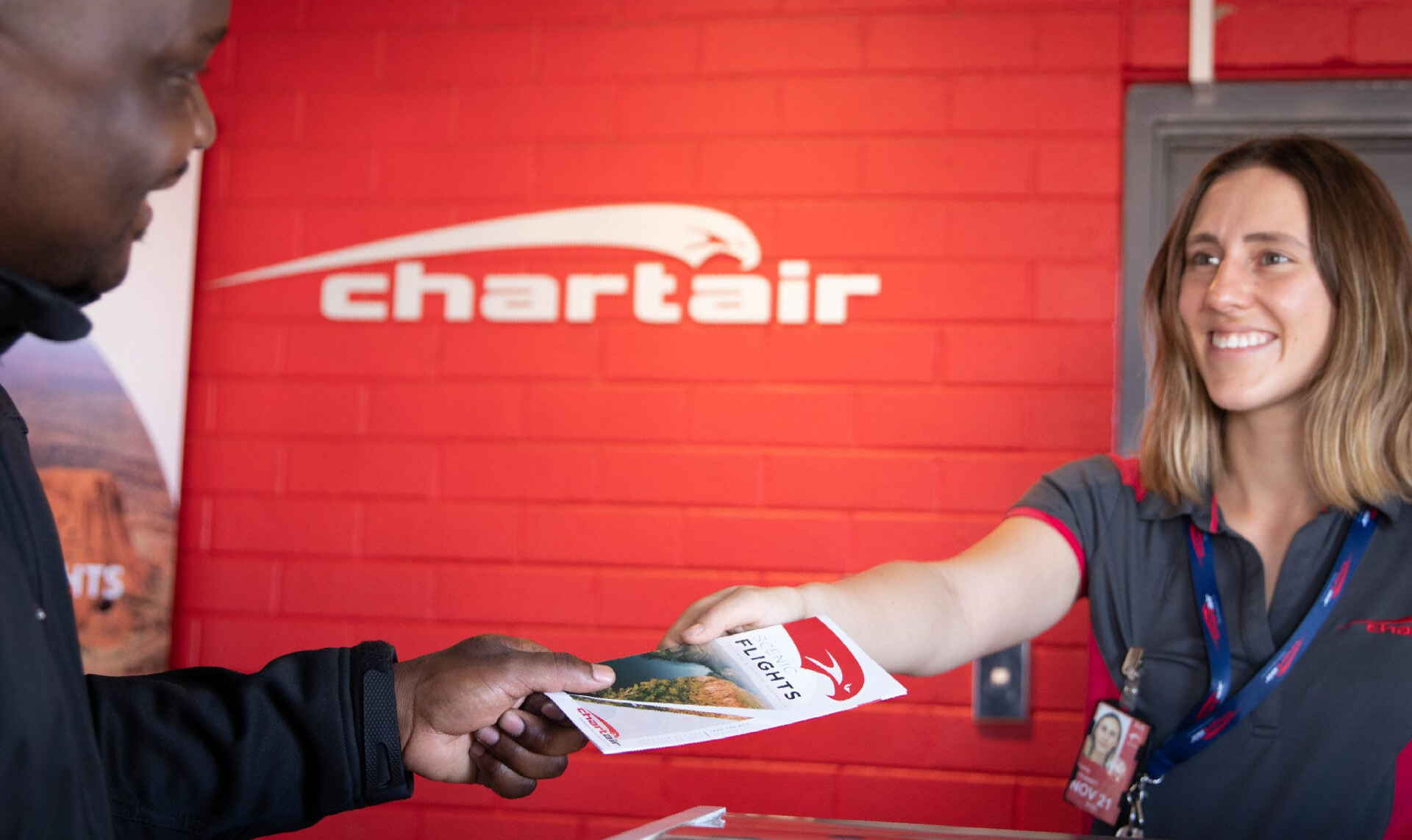 A female ground staff is handing over a brochure to a passenger