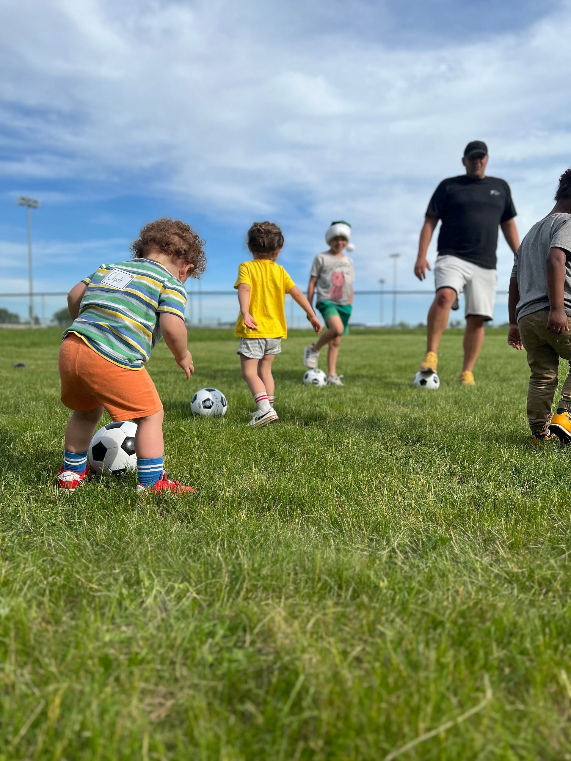 Preschool-aged children practicing soccer on a grass field with a coach guiding them during a Tiny Strikers MN session