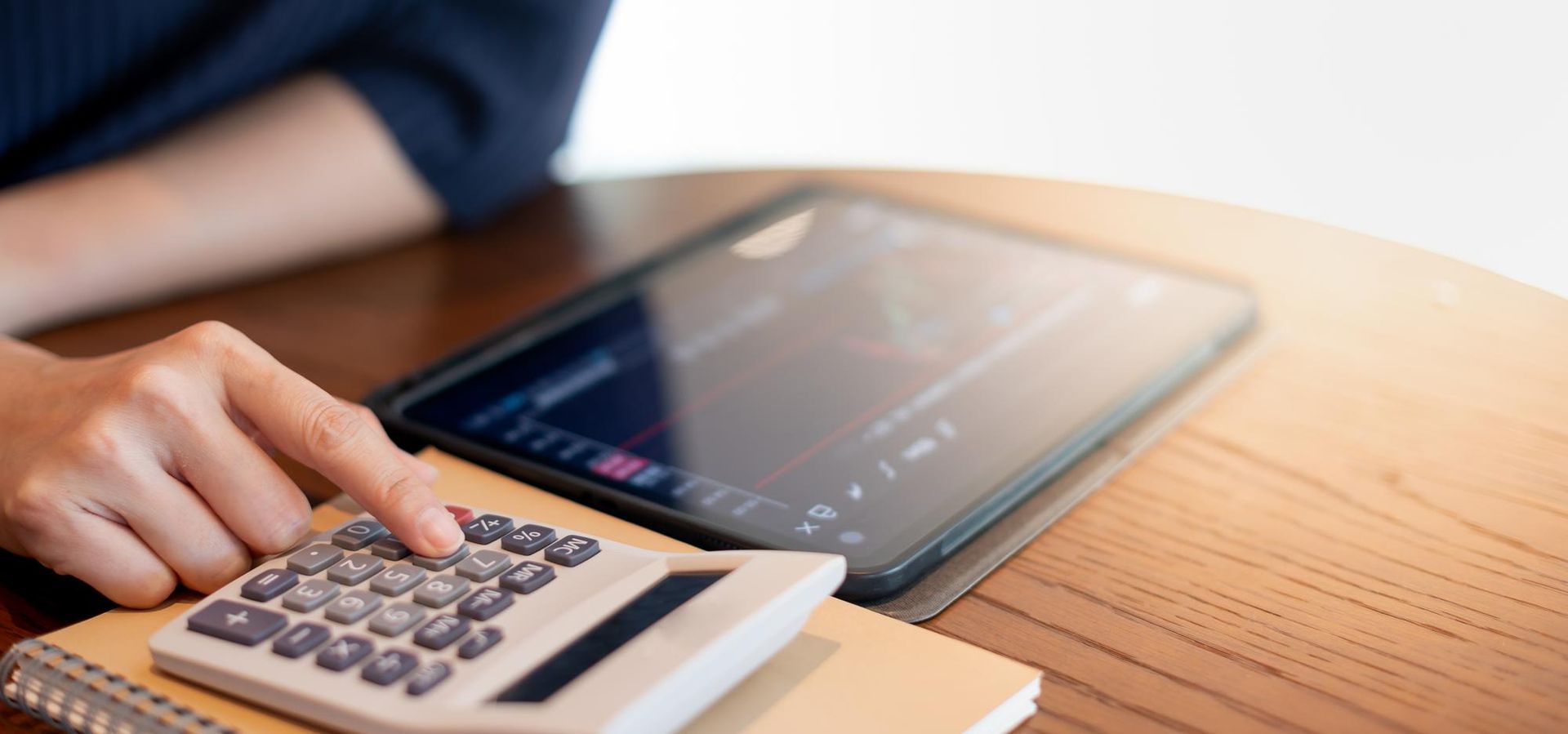 Person using a calculator with a tablet on a wooden table.